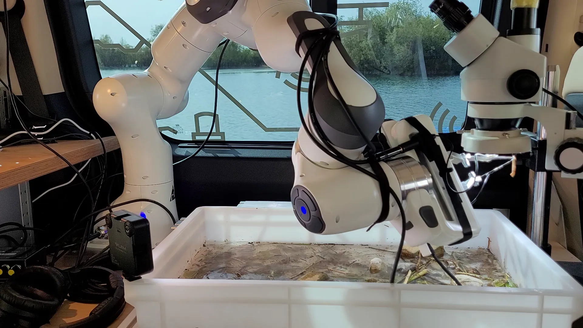 Environmental robot carefully grasping a small aquatic organism and positioning it beneath a microscope for remote microscopy.