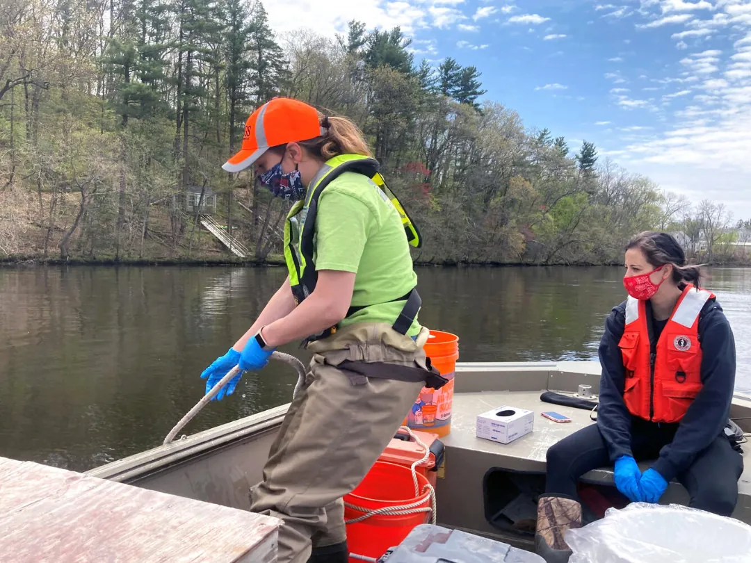Environmental experts are manually using devices from a small boat.