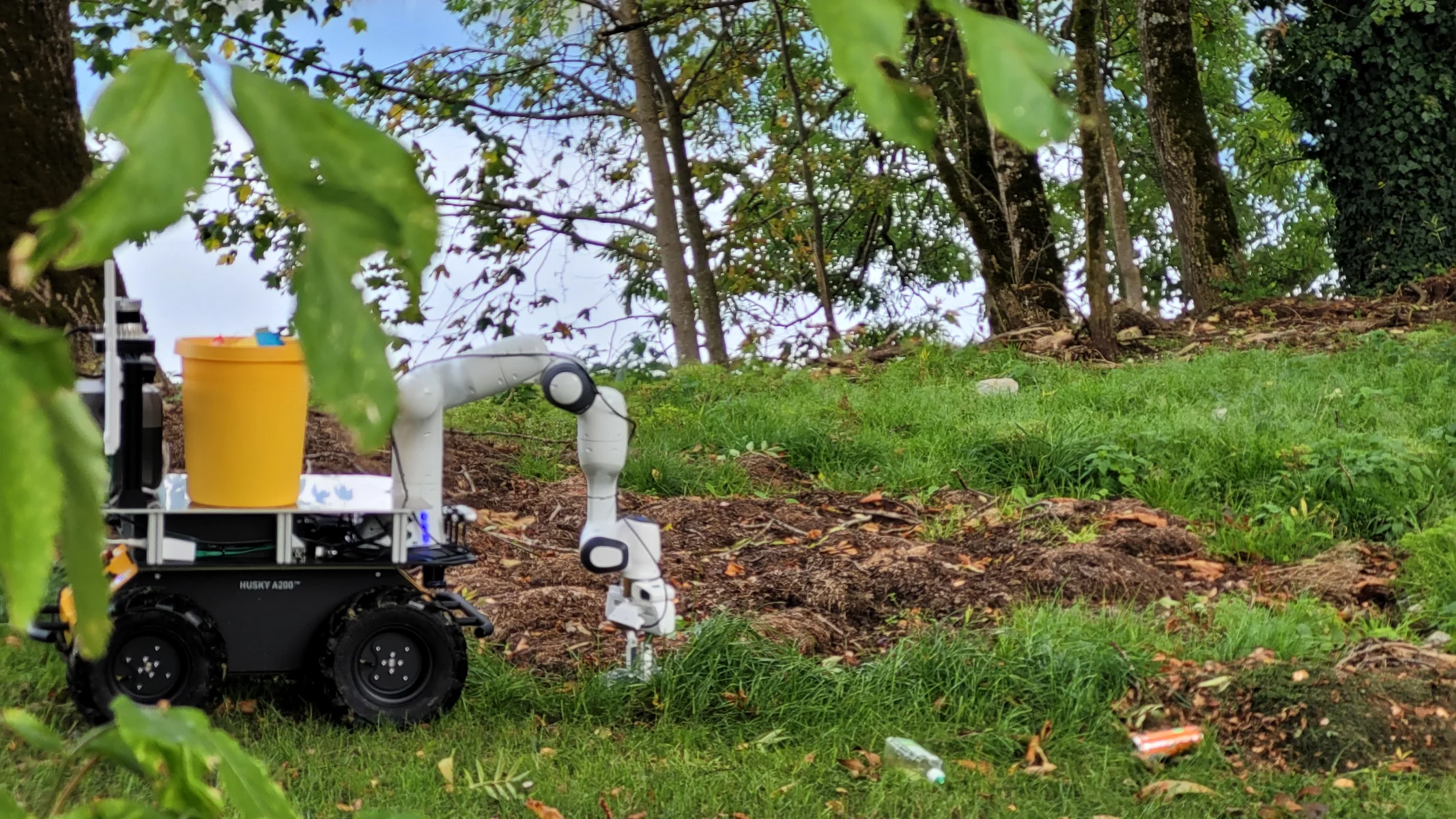 Ground robot in a forest area picking up litter with a robotic arm.